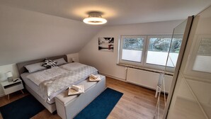 Une chambre à coucher comprenant un lit, une table de chevet, une lampe, une fenêtre, un radiateur et une vue sur l’extérieur.