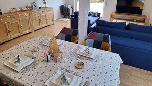 Un coin repas avec une table dressée pour quatre personnes, un buffet en bois, un téléviseur et, au fond, un canapé bleu.