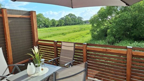 Une terrasse avec une table et des chaises, un grand parasol et une vue sur un champ verdoyant.