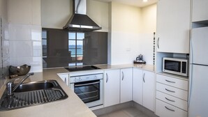 Una cocina moderna con armarios blancos, extractor de acero inoxidable, horno empotrado, microondas y un lavamanos con grifo.