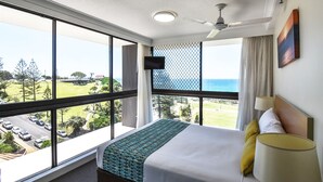 Habitación de hotel con una cama grande, ventilador de techo, televisor montado en la pared y vistas al océano y un campo de golf.