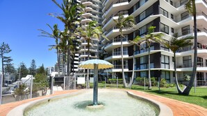 Un hotel moderno con zona de piscina en la azotea, que incluye una fuente y una sombrilla.