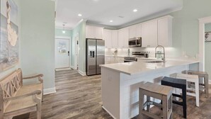 A spacious kitchen with white cabinets, a stainless steel refrigerator, and a large island with bar stools. - Bayfront Home with Beach Access (Gulf Shores)