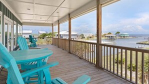 A covered outdoor deck with turquoise chairs and tables, overlooking a body of water and a marina. - Bayfront Home with Beach Access (Gulf Shores)