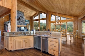 A spacious kitchen with wooden cabinets, a stone wall, and large windows offering a view of the outdoors.