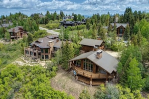 A large wooden cabin with a deck, surrounded by dense forest.