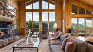 A log cabin interior with a stone fireplace, large windows, a sofa, and a coffee table. - Abode at American Flag, private hot tub, sauna, panoramic views (Park City)