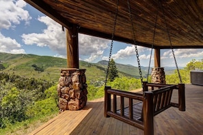 A wooden deck with a swing, stone pillar, and a view of a mountainous landscape.