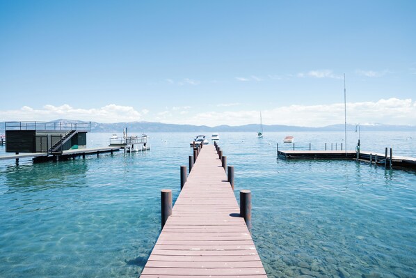 Une jetée en bois s’avance sur un lac aux eaux d’un bleu limpide, avec des bateaux amarrés de chaque côté.