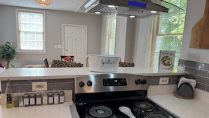 A modern kitchen with a stainless steel stove, a white pot labeled "Gourmet," and a cookbook titled "The Yoga Kitchen." - Pleasantly Charming 2-bedroom duplex in  Wynnton Village Historic District. (Columbus)