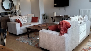 A modern living room with two sofas, a coffee table, a TV, and a dining area. - Pleasantly Charming 2-bedroom duplex in  Wynnton Village Historic District. (Columbus)