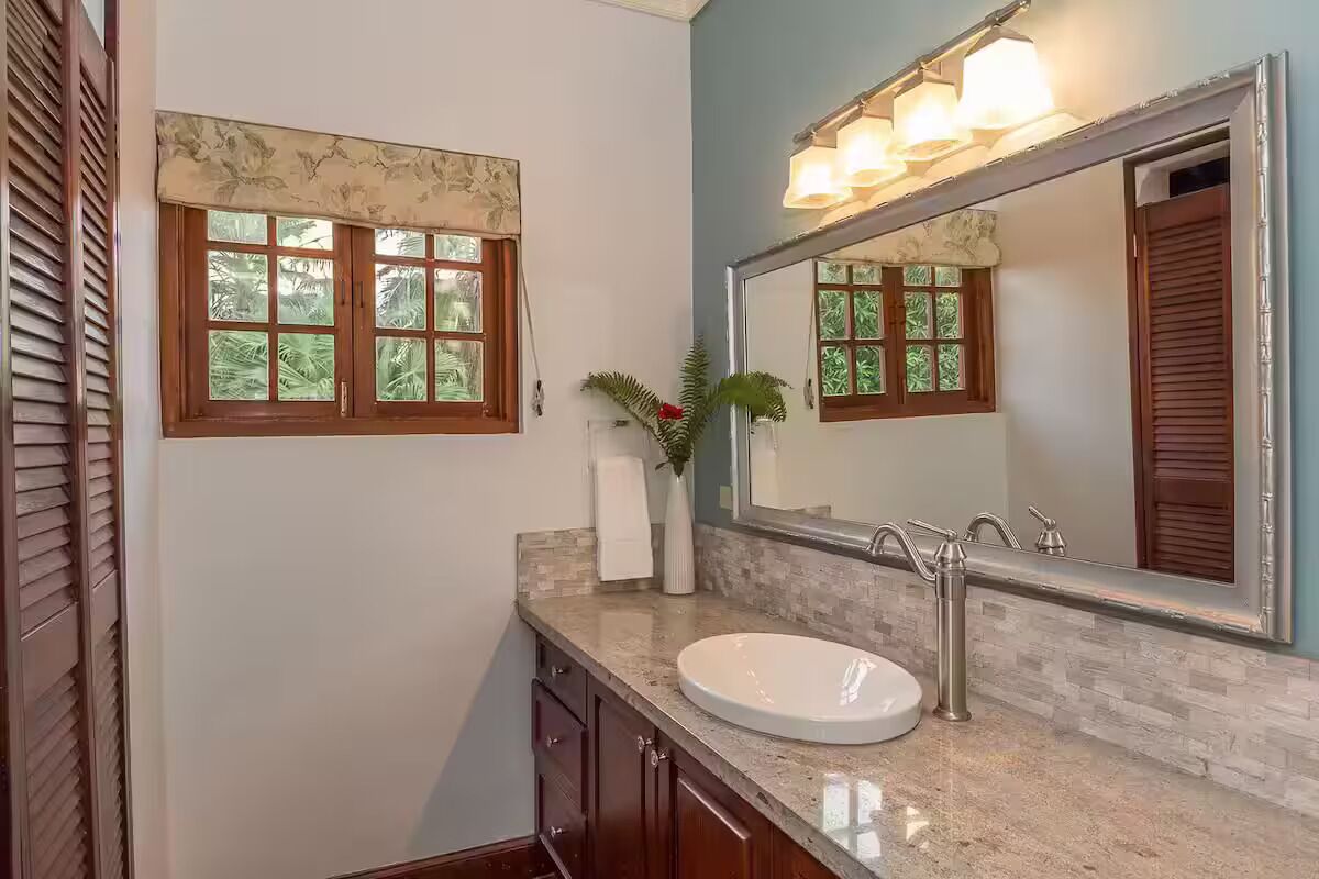 Un baño con un lavamanos blanco, un espejo grande y una ventana con un adornado floral.