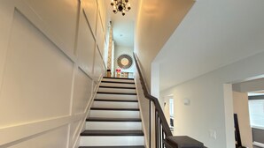 Una escalera con escalones de madera oscura y barandillas negras que conduce a una habitación con pared blanca y un aplique de techo decorativo.