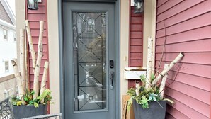 Una puerta principal con un panel de vidrio, un buzón y dos macetas.