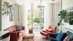 Een moderne woonkamer met leren banken, een salontafel en een groot raam met uitzicht op een bakstenen gebouw en groen buiten.