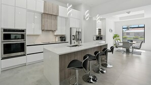 Una cocina moderna con armarios blancos, electrodomésticos de acero inoxidable y una isla central con taburetes de bar.