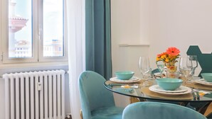 A dining area with teal chairs, a glass table, and a view of a building through a window. - CASA FEN historic building - King of Rome MetroA 2 bedrooms 2 bathrooms (Unknown)