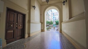 A hallway with a double wooden door, a tiled floor, and an arched doorway leading to an outdoor area with buildings and greenery. - CASA FEN historic building - King of Rome MetroA 2 bedrooms 2 bathrooms (Unknown)