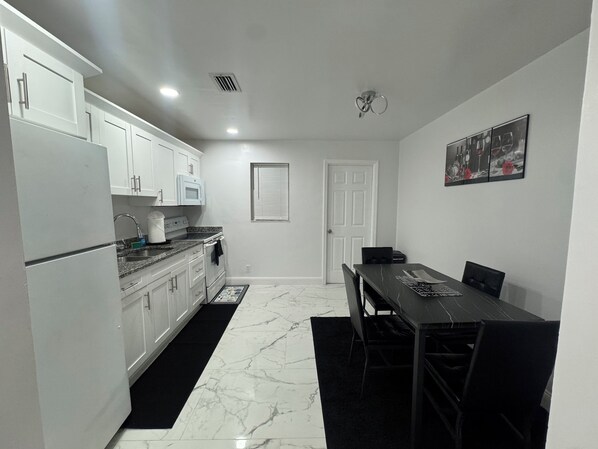 A modern kitchen with white cabinets, a black countertop, and a dining area with a table and chairs. - At Home in the Heart of West Palm Beach (West Palm Beach)