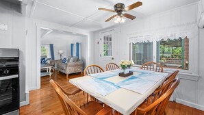 A dining area with a table set for six, a ceiling fan, and a view of the outdoors.