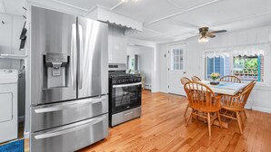 A modern kitchen with stainless steel appliances, a dining area with wooden chairs, and a ceiling fan.