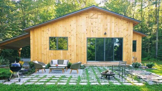 Una cabaña de madera con un patio que incluye mobiliario exterior, una parrilla y un hogar para la leña.
