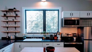 Una cocina moderna con un amplio ventanal, electrodomésticos de acero inoxidable y estantes de madera.