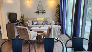Una sala de estar moderna con un sofá, una mesa de centro, sillas, un televisor y un ventanal con cortinas.