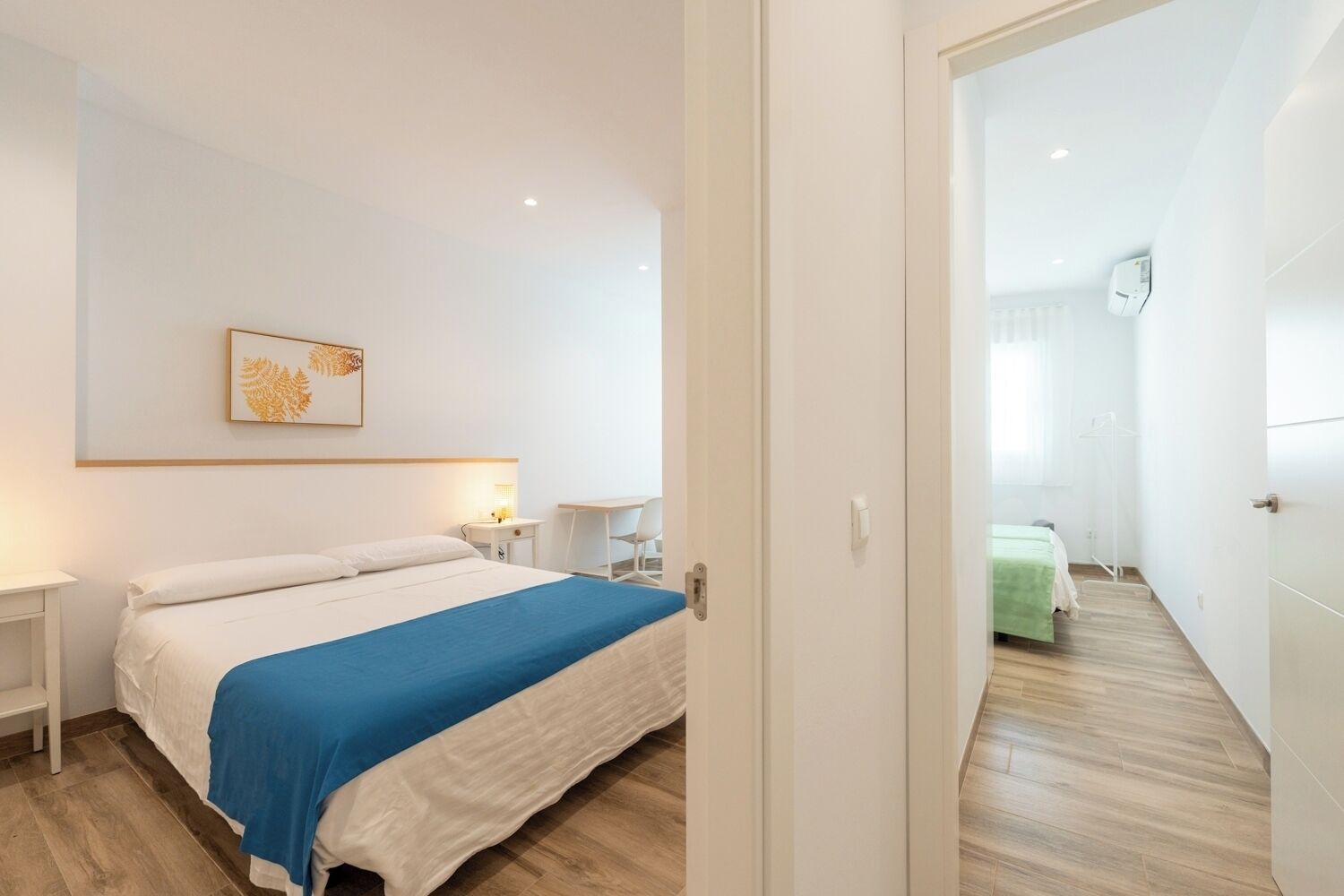 Ein modernes Hotelzimmer mit einem großen Bett, einem Schreibtisch und einem Sessel. Eine Tür führt in einen weiteren Raum.