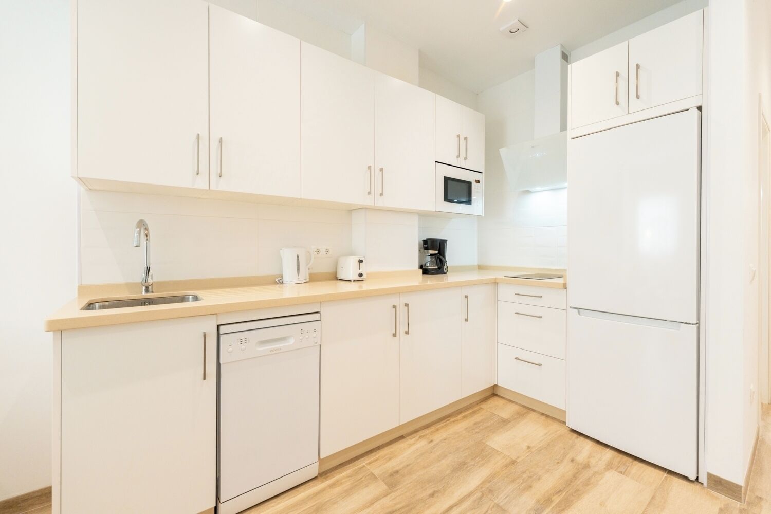 A modern kitchen with white cabinets, a dishwasher, a microwave, and a refrigerator.