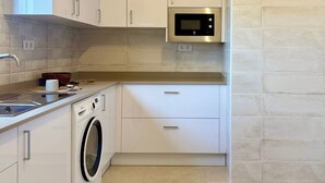 Une cuisine compacte avec des meubles blancs, un four à micro-ondes en acier inoxydable, un lave-linge et un évier.