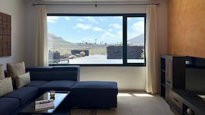 Un salon moderne avec un canapé bleu foncé, une table basse en verre et un téléviseur à écran plat. Une grande fenêtre offre une vue sur un paysage montagneux.