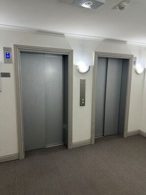 A hallway with two elevator doors, a blue accessibility sign, and a light switch on the wall.