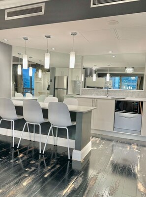 Une cuisine moderne dotée d’un îlot central, de chaises blanches et de luminaires suspendus.