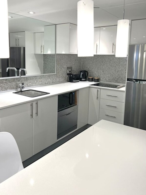 A modern kitchen with white cabinets, a stainless steel refrigerator, a built-in oven, and a coffee maker.