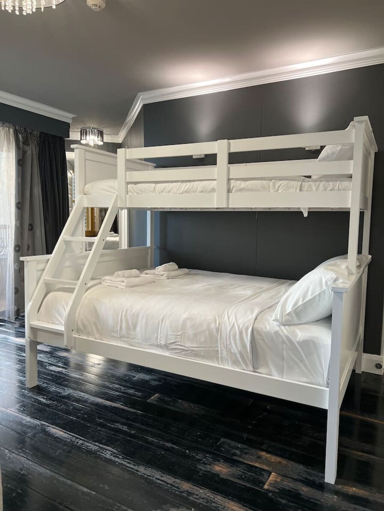A bunk bed with white bedding and a ladder, set against a dark wall with a chandelier.