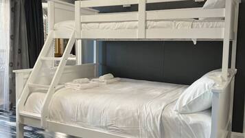 A bunk bed with white bedding and a ladder, set against a dark wall with a chandelier.