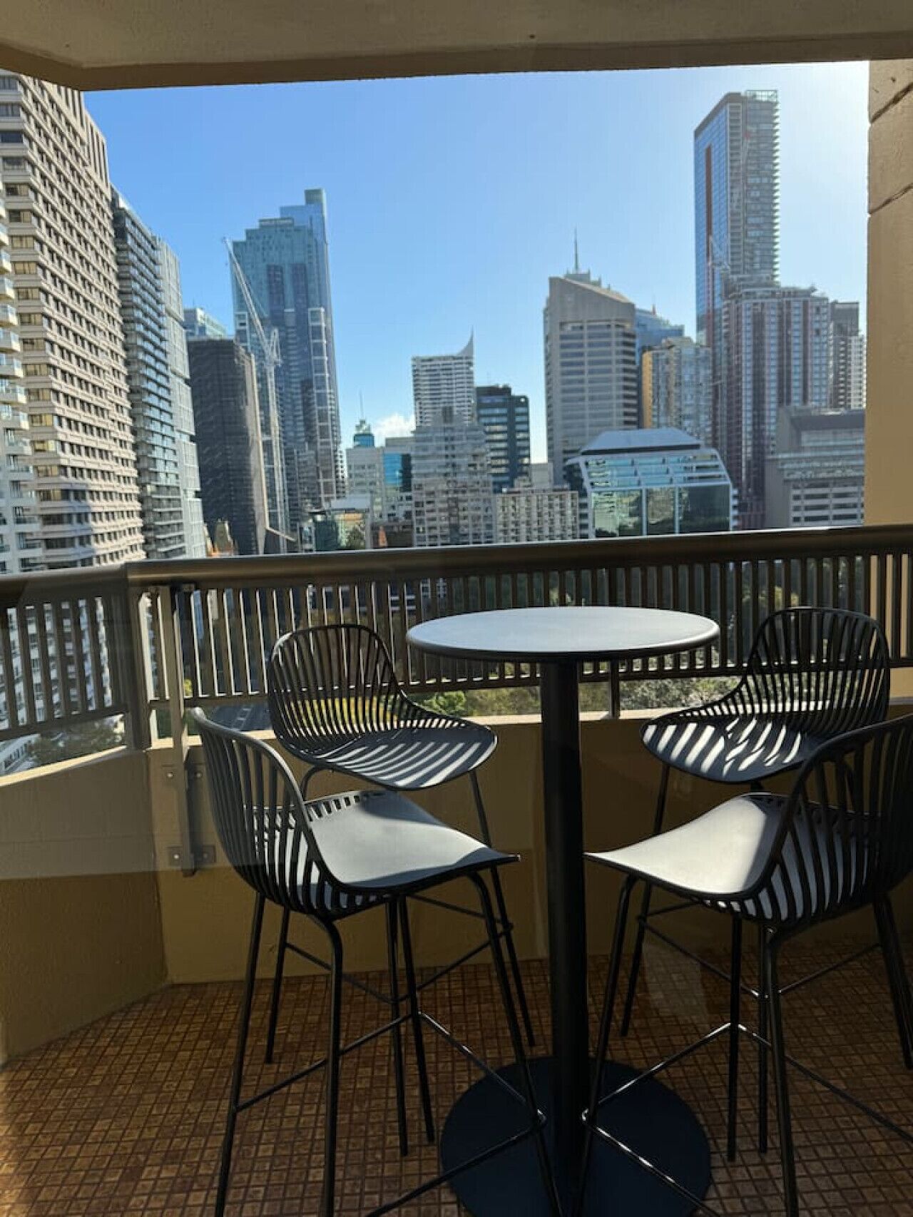 A balcony with a round table and four chairs, overlooking a cityscape with tall buildings.