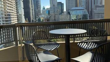 A balcony with a round table and four chairs, overlooking a cityscape with tall buildings.