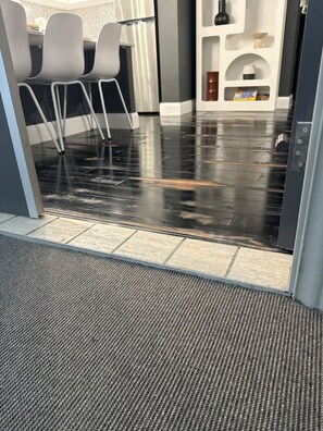 A wet floor with a textured mat at the entrance, a seating area with chairs, and a white wall with a shelf.