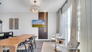 Ein moderner Essbereich mit einem Holztisch, schwarzen und weißen Stühlen, einem gemusterten Teppich und einem großen Fenster mit Vorhängen.