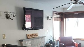 A living room with a fireplace, a television mounted on the wall, and a ceiling fan.