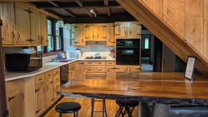 Una cocina con gabinetes de madera, un horno negro y una encimera de granito. Hay dos taburetes y una lámpara colgante.