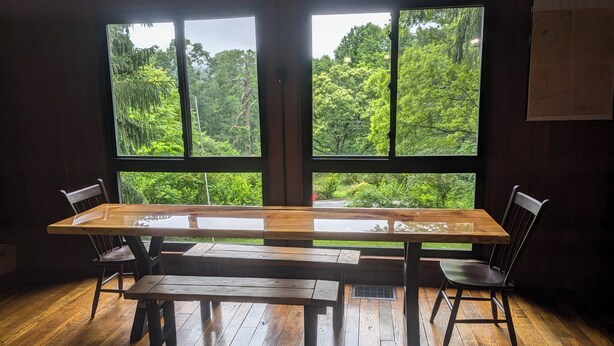 Una habitación con una gran mesa y sillas de madera, ventanas amplias con vistas a vegetación exuberante.