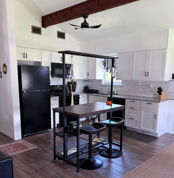 A modern kitchen with white cabinets, a black refrigerator, a wooden table, and a ceiling fan.