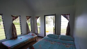 A room with two single beds and a larger bed, each with floral bedding. There are windows with curtains, and a door leading outside.