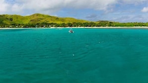 A coastal landscape with clear turquoise waters, a boat in the distance, and green hills in the background.