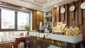 Un comptoir de réception d’hôtel avec un revêtement en marbre, des panneaux en bois, des horloges et un arrangement floral.