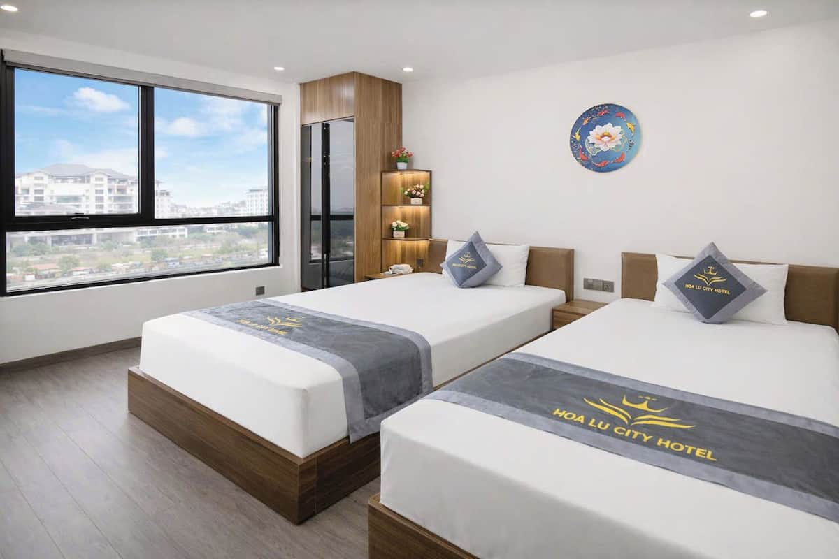 Een hotelkamer met twee bedden, een kledingkast, een nachtkastje, een decoratief bord en uitzicht op de stad.