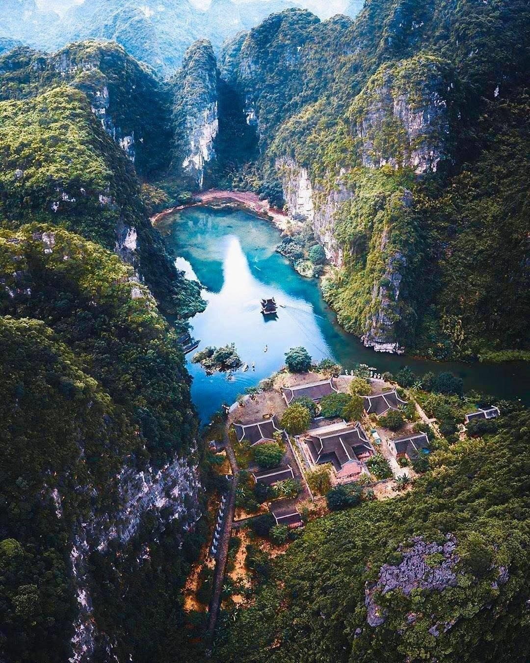 An aerial view of a mountainous area with a clear blue lake, surrounded by dense forest and traditional buildings.